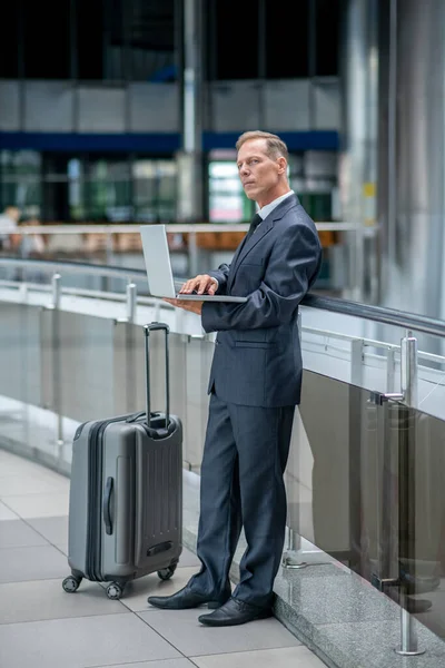 Man werkend op laptop staand met koffer — Stockfoto