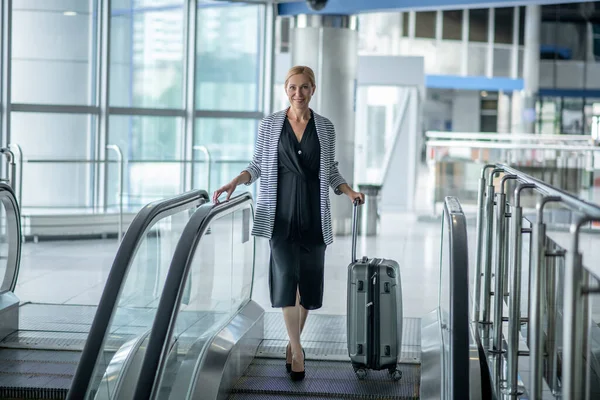 Mujer con maleta de pie en la escalera mecánica en la terminal — Foto de Stock