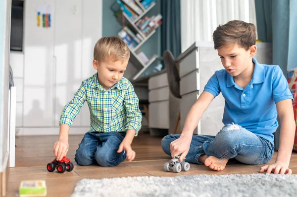 Dois irmãos brincando com carros modelo dentro de casa — Fotografia de Stock