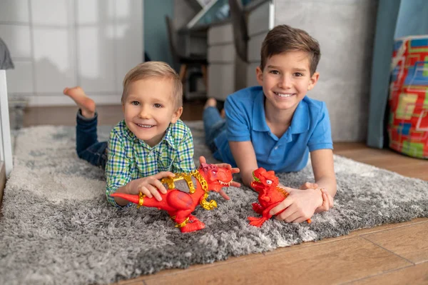 Cheerful boys with toy dinosaurs resting on the floor — Stock Photo, Image