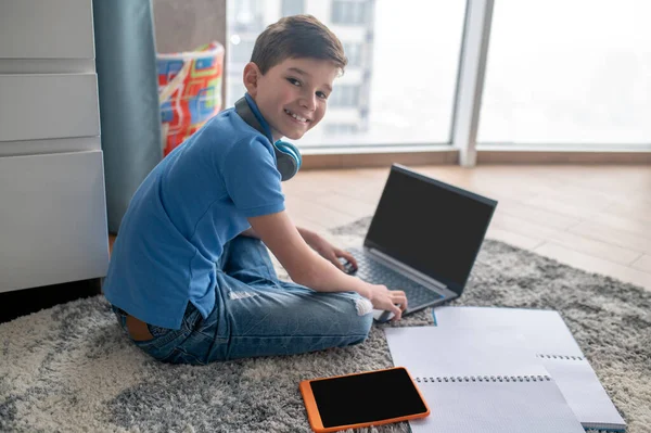 Alumno alegre sentado en la alfombra durante su lección en línea — Foto de Stock