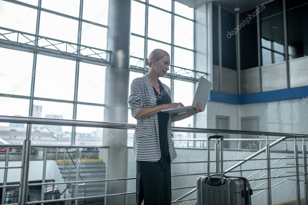 Woman looking at laptop standing near suitcase