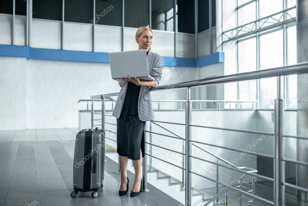 Woman with laptop standing near suitcase in terminal