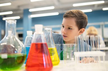 Çocuk renkli sıvılarla mataraları inceliyor.