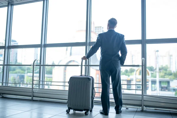 Человек с чемоданом стоит и смотрит на окно в терминале — стоковое фото