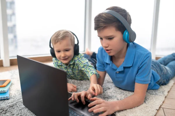 Irmãos em fones de ouvido olhando para o laptop no chão — Fotografia de Stock