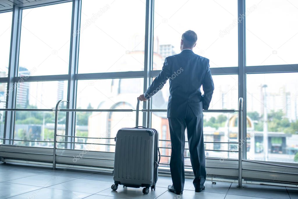 Man with suitcase standing looking at window in terminal
