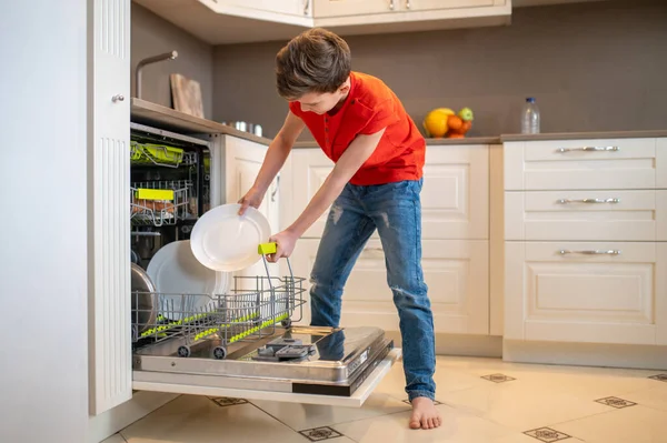 Menino colocando pratos em uma máquina de lavar louça aberta — Fotografia de Stock