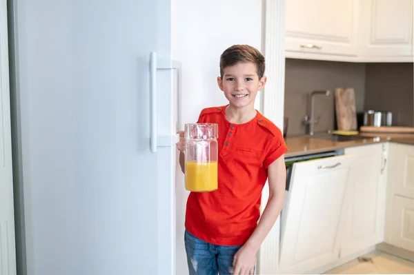 Criança agradável segurando um jarro com suco de laranja — Fotografia de Stock