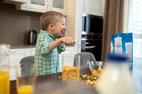 Junge sitzt am Küchentisch zwischen verstreuten Frühstücksflocken — Stockfoto