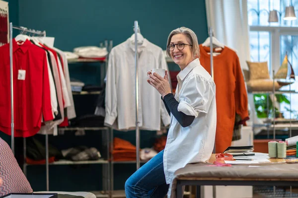 Femme avec tasse accroupie sur la table souriant à la caméra — Photo