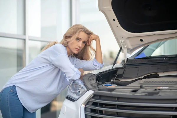 Woman sad looking at camera touching car hood — Stock Photo, Image