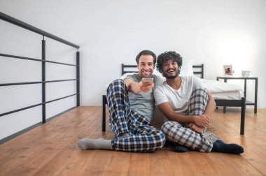 İki neşeli adam cep telefonunu kanal sörfü için kullanıyor.