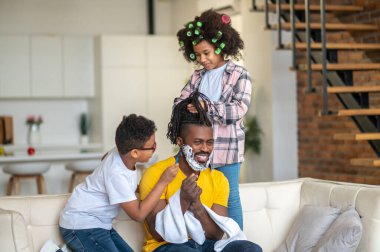 Çocuklar evde babalarını tıraş edip tarıyorlar.