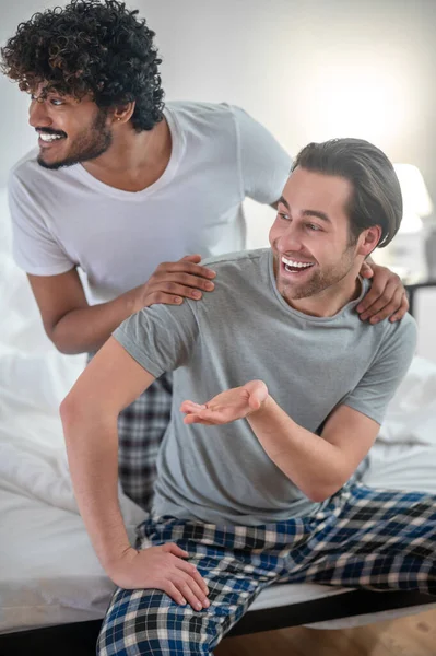 Cheerful biracial gay couple sitting in the bedroom — Stock Photo, Image