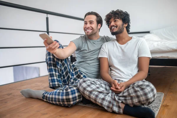 Fröhliches schwules Paar sitzt beim Kanalsurfen auf der Bodenmatte — Stockfoto