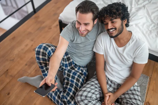 Casal masculino mudando de canais de TV a partir do celular — Fotografia de Stock