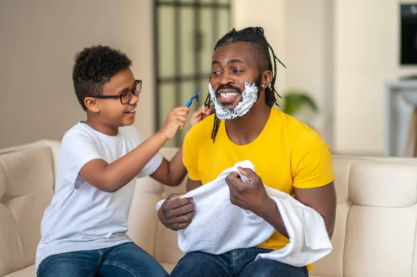 소파에 앉아 아버지를 면도 하는 소년 — 스톡 사진