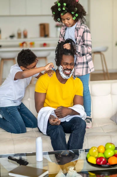 A fiú borotválja a nevető apját és a lányát befonja. — Stock Fotó