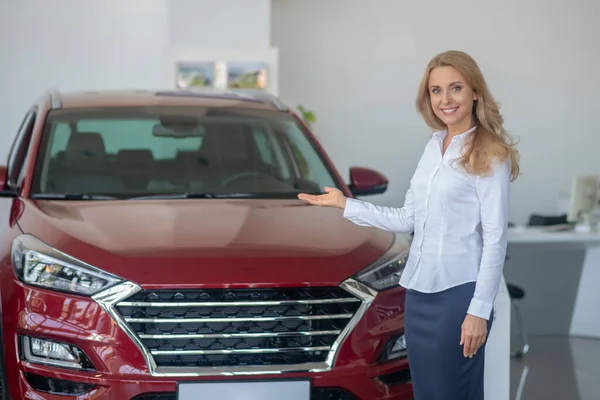 Kameraya gülümseyen arabayı işaret eden kadın.