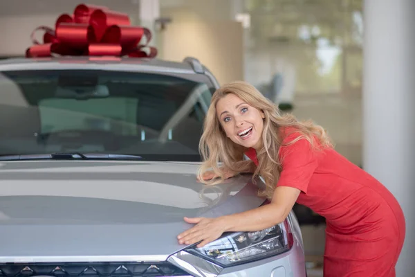 Delighted woman hugging new car in showroom