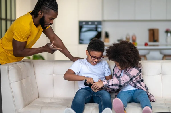 Mann gestikuliert und schaut Kinder auf Couch an — Stockfoto