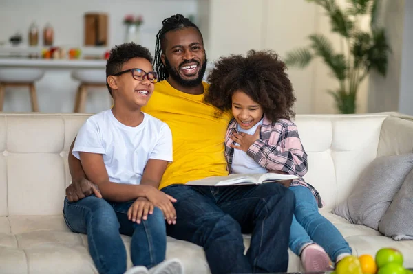 Dad with book hugging children laughing sitting on sofa — Stock Photo, Image