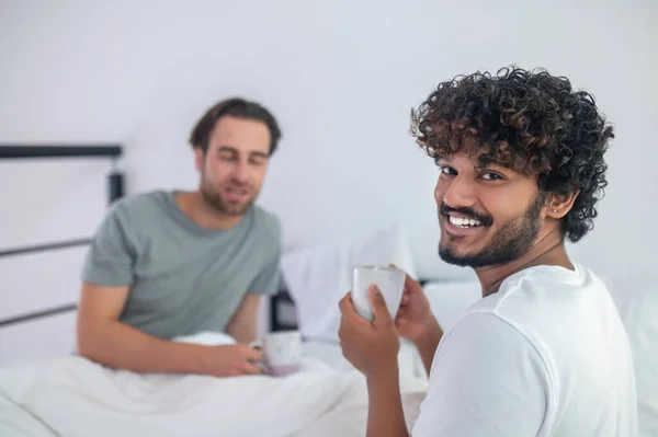 Pria minum kopi dengan pacarnya yang mengantuk di kamar tidur — Stok Foto