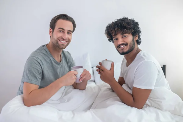 Feliz pareja gay bebiendo café en su dormitorio — Foto de Stock