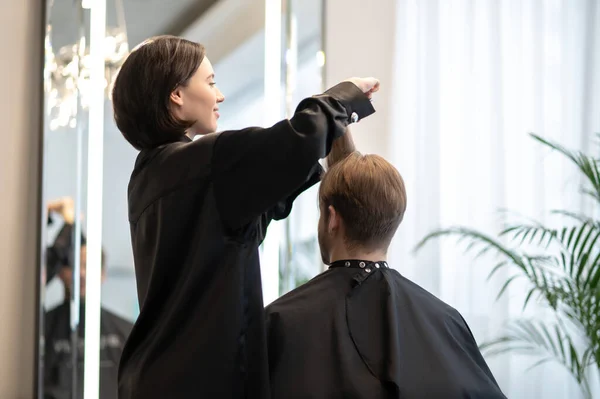 Peluquería de cabello oscuro trabajando en un corte de pelo elegante — Foto de Stock