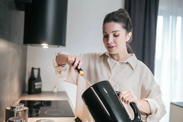 Een jonge donkerharige vrouw met een gebroken ketel in haar handen. — Stockfoto