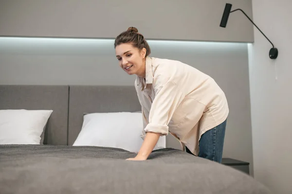 Een jonge vrouw die haar bed opmaakt en er positief uitziet — Stockfoto
