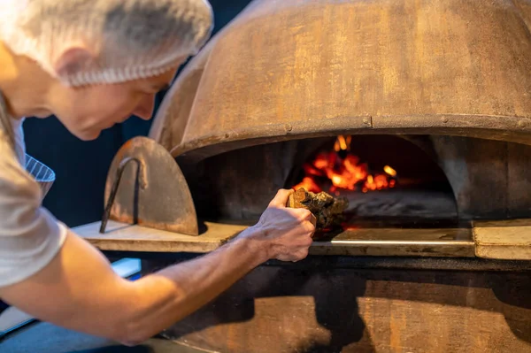 Человек, разжигающий огонь в печи в итальянской пекарне — стоковое фото