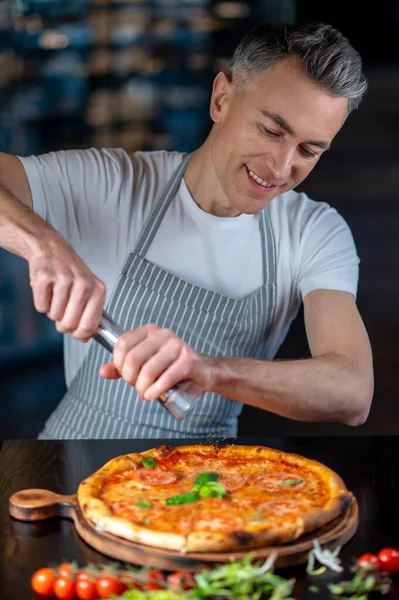 Önlüklü bir adam vişneli domatesli vejetaryen pizza yapıyor. — Stok fotoğraf