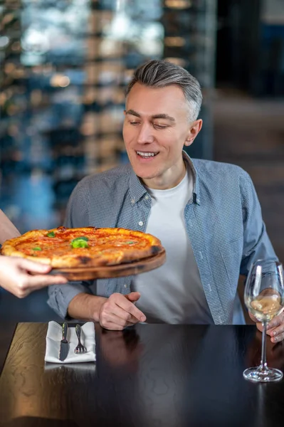 Een man zit in een café en maakt zich klaar voor het eten van een heerlijke pizza — Stockfoto