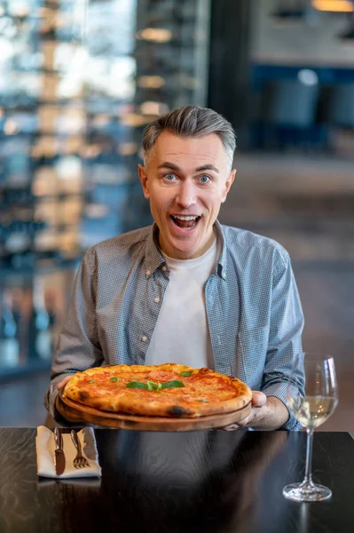 Een man die pizza eet en er opgewonden uitziet — Stockfoto