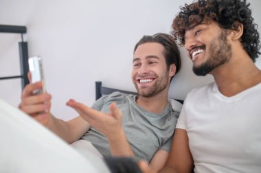 Neşeli adam cep telefonuyla arkadaşına fotoğraf gösteriyor.