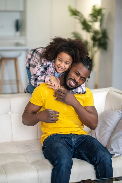 Girl hugging behind shoulders of dad sitting on couch