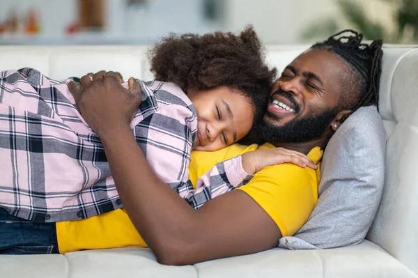 Happy man hugging daughter lying on sofa — Stock Photo, Image
