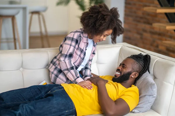 Dívka dotýká smějící se táta ležel na pohovce — Stock fotografie