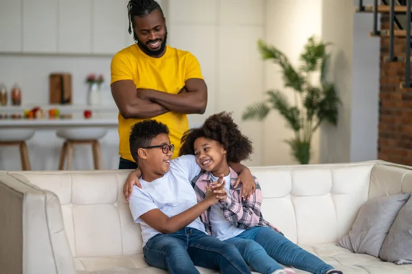 Papá de pie viendo niños alegres sentados en el sofá —  Fotos de Stock