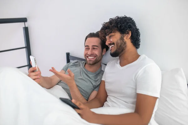 Веселий чоловік вказує на екран свого мобільного телефону своєму хлопцеві — стокове фото