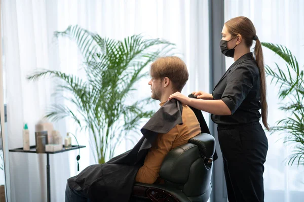 Langhaarige Friseurin arbeitet mit einem männlichen Kunden bei der Schönheitsschlachtung — Stockfoto