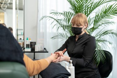 Koruyucu maskeli bir kadın güzellik salonunda müşteriye masaj yapıyor.