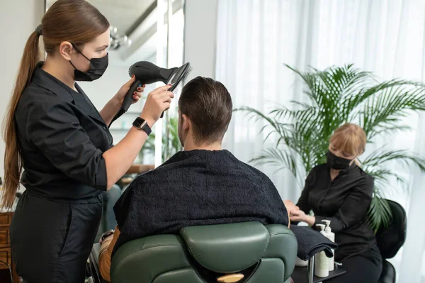 Koruyucu maskeli kuaför müşteriye saç kurutuyor. — Stok fotoğraf