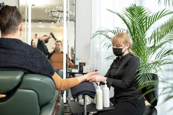 Mujer en máscara protectora masajeando manos al cliente en un salón de belleza — Foto de Stock