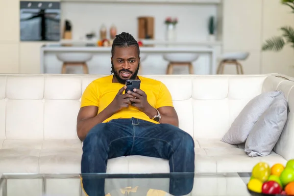 Hombre de piel oscura mirando teléfono inteligente en el sofá — Foto de Stock