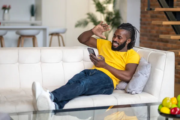 Чоловік дивиться на смартфон, піднімаючи руку у вітальні — стокове фото