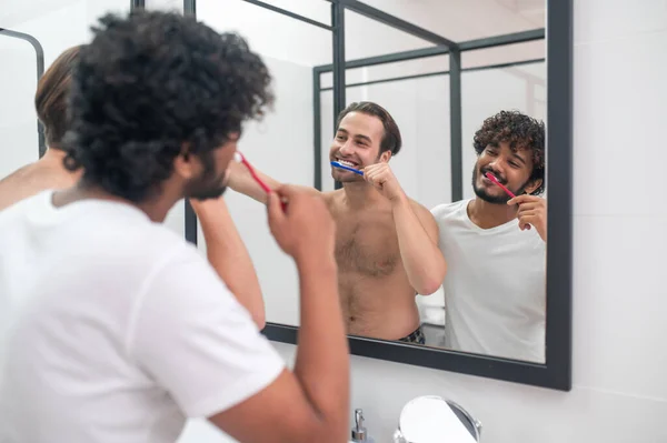 Веселый мужчина без рубашки и его парень чистят зубы вместе — стоковое фото