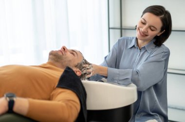 Genç adam kafa masajı yaptırırken ve rahatlamış görünürken koltukta oturuyor.